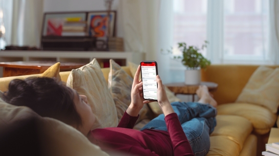 Frau liegt auf Couch nutzt am Smartphone die Oberbank Banking App