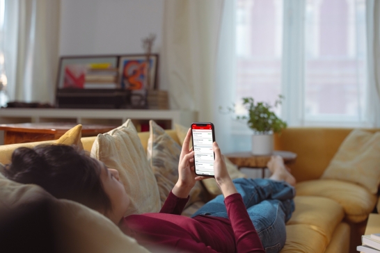 Frau liegt auf der Couch und nutzt die Oberbank Banking App am Smartphone