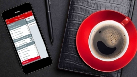 Eine Kaffeetasse, ein Notizbuch und ein Handy mit geöffneter Oberbank Business App