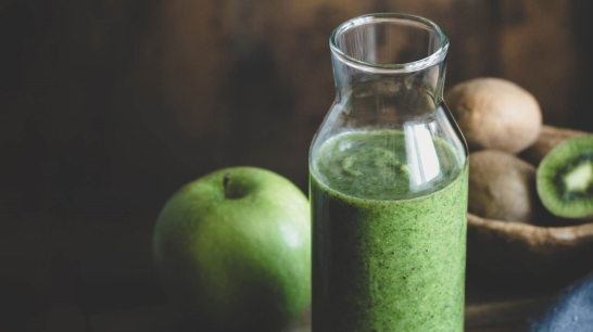Grünes Obst im Hintergrund mit Karaffe gefüllt mit grünem Smoothie