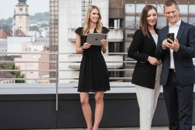Zwei Frauen und ein Mann mit jeweils einem Handy und Tablet in der Hand
