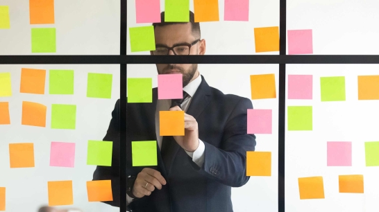 Mann ordnet Post-its auf einer Glaswand