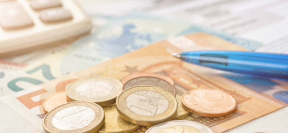 Detailansicht auf Geldscheine, Münzen, Taschenrechner und Kugelschreiber