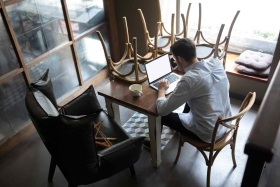 Mann sitzt an einem Tisch über einen Laptop gebeugt