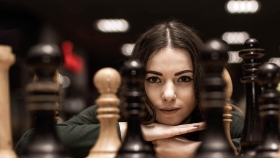 Schachbrett und Frau. Frau sieht aus dem Hintergrund durch die Schachfiguren