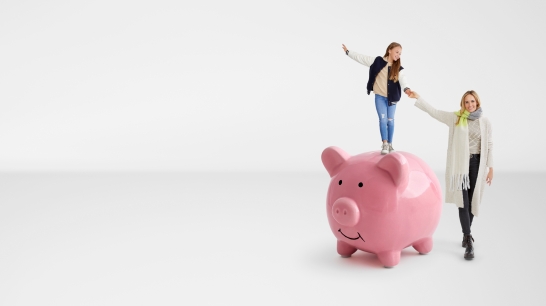 Kind steht auf rosa Sparschwein. Daneben steht eine Frau und hält ihre Hand.