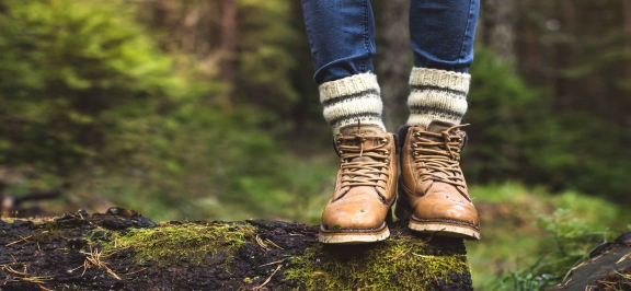 Bildausschnitt mit Beinen in Wanderschuhen, auf einem Baumstamm stehend