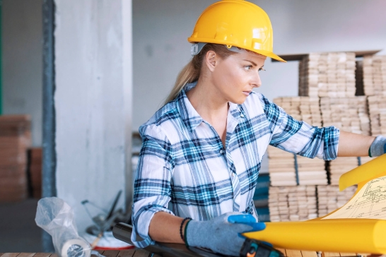 Frau mit gelben Helm auf Baustelle liest Bauplan