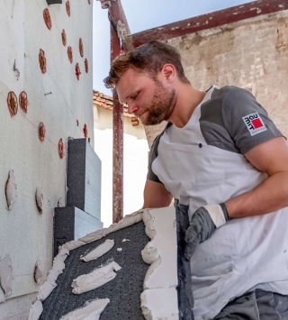 Fassadendämmung senkt Energieverbrauch und spart Geld. Mann steht bei Mauer und dämmt die Wand.